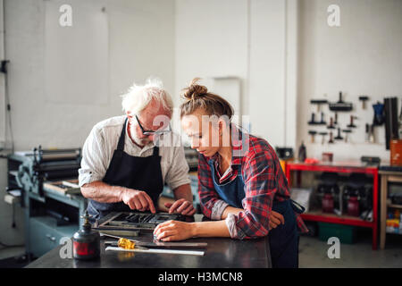 Senior craftsman working on letterpress with young craftswoman in print workshop Stock Photo