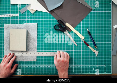 Overhead detail of hands, paper, cutting mat, ruler, scalpel and scissors in print studio Stock Photo