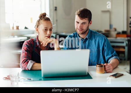 Young craftsman and craftswoman looking at laptop in print studio workshop Stock Photo