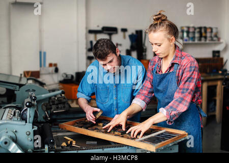 Young craftsman and craftswoman looking at letterpress letters in book arts workshop Stock Photo
