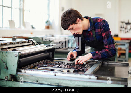 Young man working on letterpress machine in book arts workshop Stock Photo