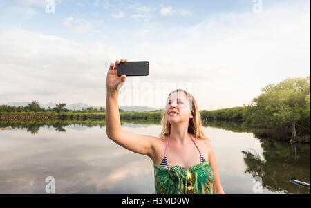 Young woman taking smartphone selfie in front of lake, Gili Meno, Lombok, Indonesia Stock Photo