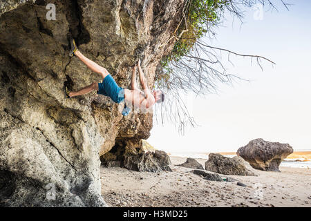 Male free climber climbing rock overhang on Pandawa Beach, Bali, Indonesia Stock Photo