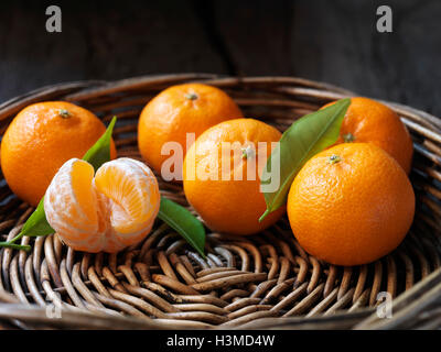 Fresh organic fruit, clementines with leaves in wicker bowl Stock Photo