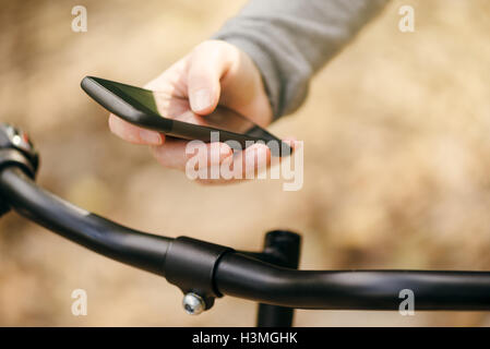 Woman using smart app on phone while riding bicycle through park during autumn season, lifestyle and technology concept Stock Photo