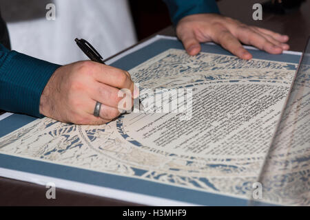 Bride and groom signing the ketubah or wedding contract outlining rights and obligations at a Jewish wedding in a close up view