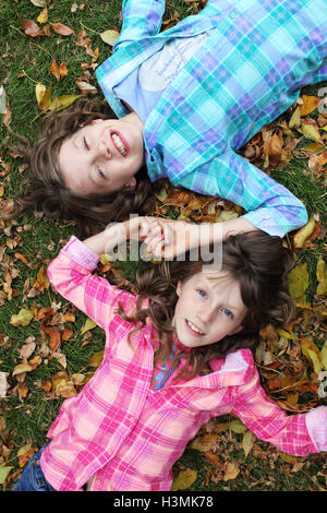 two young girls dressed in bright plaid colors laying on fall ground covered in leaves Stock Photo