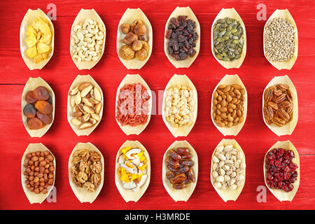 Nuts and dried fruits selection in wooden bowls on red rustic table, view from above. Stock Photo