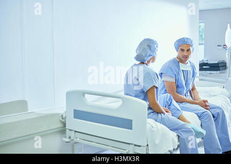 Male and female nurse sitting on bed chatting in hospital ward Stock Photo