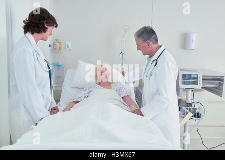 Two doctors talking to senior female patient in hospital bed Stock Photo