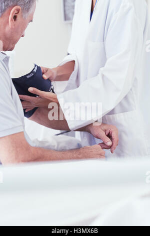 Cropped shot of female doctor using blood pressure gauge on senior male patient on hospital bed Stock Photo