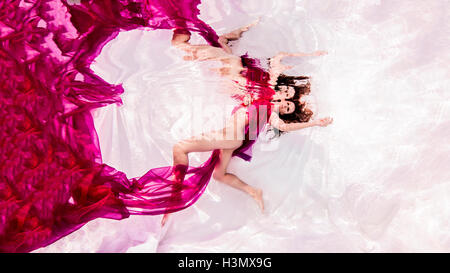 Underwater view of woman draped in sheer fabric, floating towards water surface Stock Photo