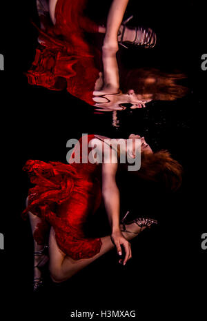 Underwater view of girl wearing red dress and high heeled shoes, reflected in water surface