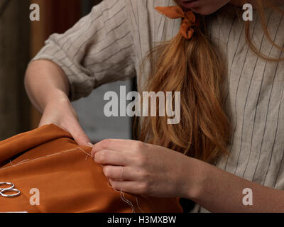Cropped close up of young female designer's hands sewing orange fabric Stock Photo