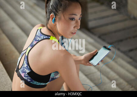 Woman sitting on steps wearing earphones holding smartphone Stock Photo