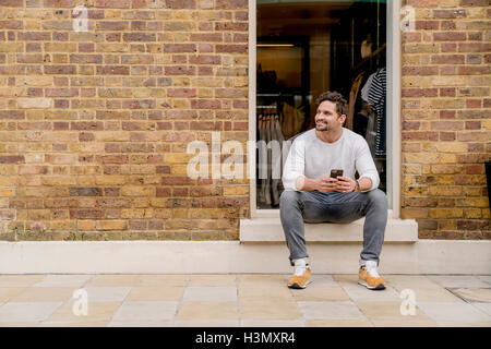 Young man with smartphone sitting on doorstep, Kings Road, London, UK Stock Photo