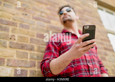 Low angle view of young man leaning against brick wall holding smartphone Stock Photo