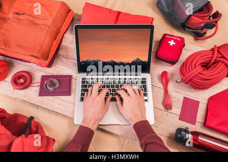 Overhead view of man's hands typing on laptop whilst preparing climbing equipment for travel Stock Photo