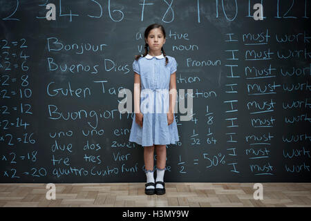 Portrait of schoolgirl standing in front of large chalkboard with schoolwork chalked on it Stock Photo