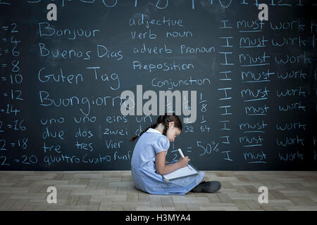 Schoolgirl sitting studying in front of large chalkboard with schoolwork chalked on it Stock Photo