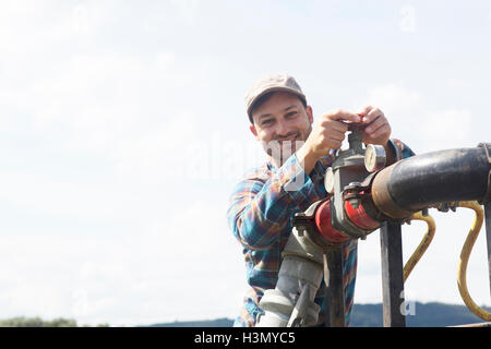 Man opening valve on industrial piping, looking at camera smiling Stock Photo