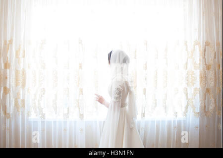 muslim woman in a white headscarf looking out the window Stock Photo