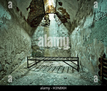 Crumbling abandoned prison cell with cot Stock Photo