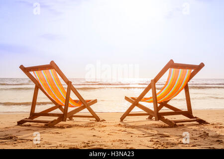 Two deckchairs on the beach at sunset with a tropical sea background Stock Photo