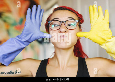 Portrait of young woman with pink hair pulling a face wearing mismatched rubber gloves Stock Photo
