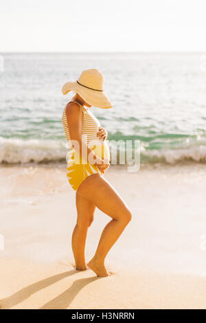 Pregnant mid adult woman wearing swimming costume holding stomach Makua beach, Hawaii, USA Stock Photo