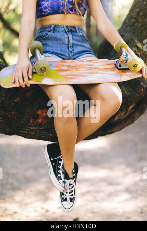 Woman with skateboard sitting on tree Stock Photo