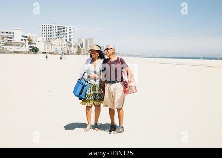 Senior couple walking on beach, carrying bags for picnic, Long Beach, California, USA Stock Photo