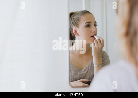 Mirror image of young woman applying lipstick Stock Photo