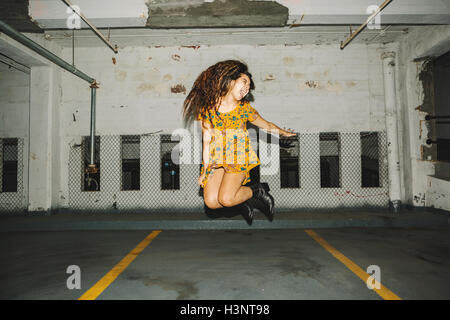 Young woman jumping mid air in indoor parking lot Stock Photo