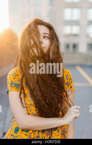 Portrait of young girl pulling long wavy hair across face in parking lot Stock Photo