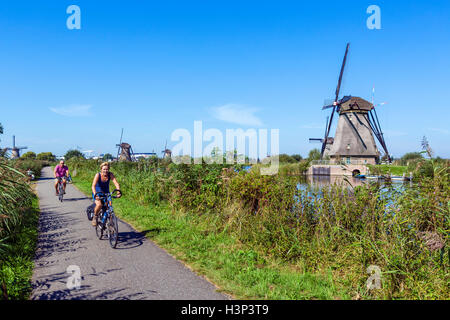 Cyclists by the historic windmills at Kinderdijk, Molenwaard, near Rotterdam, Netherlands Stock Photo