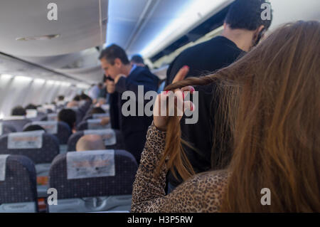 Travel scene, passengers prepare to leave the airplane, man puts coat, woman straightens her hair. Stock Photo