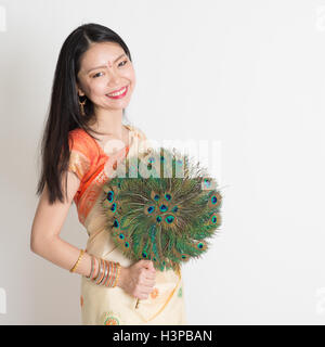 Portrait of young mixed race Indian Chinese woman in traditional sari dress, holding peacock feathers fan and looking at camera, Stock Photo
