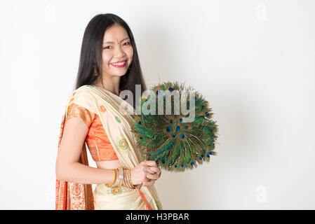 Portrait of young mixed race Indian Chinese girl in traditional sari dress, holding peacock feathers fan and looking at camera, Stock Photo