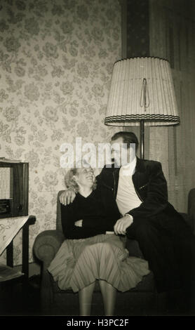 BERLIN, GERMANY - CIRCA 1960s: man and woman posing on a chair in the living room, on the background of a floor lamp Stock Photo
