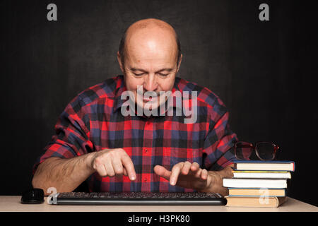 elderly man in a plaid shirt home printing a message on the keyboard. Stock Photo
