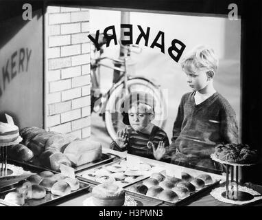 1930s 1940s TWO BOYS LOOKING IN BAKERY SHOP WINDOW AT DESSERTS ONE BOY PRESSING HANDS AND NOSE AGAINST WINDOW Stock Photo