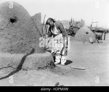 1930s NATIVE AMERICAN INDIAN WOMAN BAKING BREAD IN OUTDOOR HORNO OVEN SANTA CLARA PUEBLO NEW MEXICO USA Stock Photo