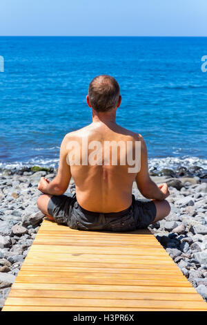 Middle aged man meditating at coast and ocean Stock Photo
