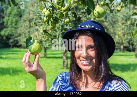 European woman wearing blue hat holding pear in orchard Stock Photo