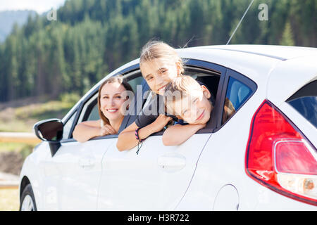 Happy young woman and her children sitting in a car and look out from windows. Family travel background image