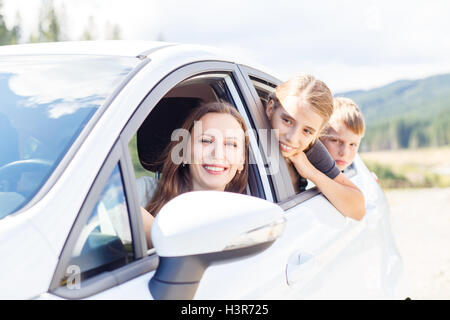 Happy young woman and her children sitting in a car and look out from windows. Family travel background image