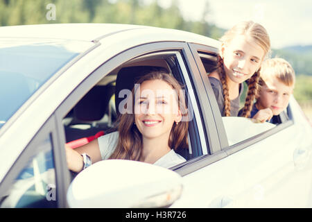 Happy young woman and her children sitting in a car and look out from windows. Family travel warm color toned image