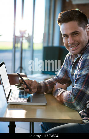 Smiling man using mobile phone with laptop on table Stock Photo