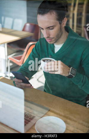 Man using mobile phone while having cup of coffee Stock Photo